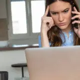 Femme soucieuse au téléphone, devant son ordinateur, envisageant de porter plainte contre une entreprise.