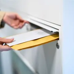 Main tenant insère des enveloppes dans une boîte aux lettres. Le délai recommandé pour la réception est important.