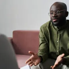 Un homme barbu en chemise verte et lunettes discute avec une personne hors champ, évoquant une rupture conventionnelle.
