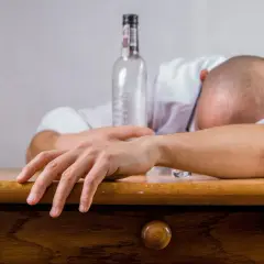 Un homme endormi sur son bureau, une bouteille vide à côté. Les conséquences de l'alcool au travail sont visibles.