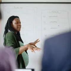 Une femme enceinte présente un tableau blanc, discutant peut-être de la réduction du temps de travail pendant la grossesse.
