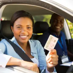 Une jeune femme souriante tient son permis de conduire, fière de sa réussite. L'auto-école veille à la répression des fraudes pour des formations honnêtes.