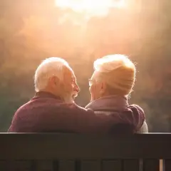 Couple âgé regardant le soleil couchant, bras autour des épaules.