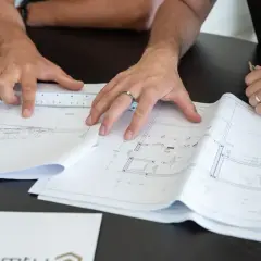 Des mains travaillent sur des plans d'architecte, une règle à la main. Comprendre ces détails est essentiel pour savoir pourquoi faire un devis précis.