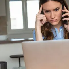 Femme soucieuse au téléphone, devant son ordinateur, envisageant de porter plainte contre une entreprise.