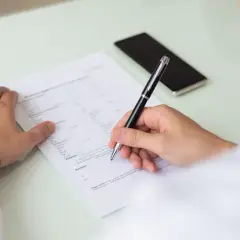 Un homme remplit un formulaire, peut-être un cerfa, pour une demande. Il utilise un stylo pour signer.