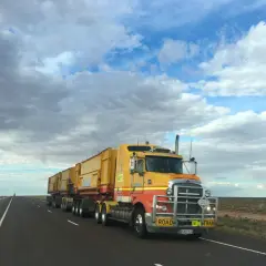Un long camion jaune, un "road train", roule sur une route déserte sous un ciel nuageux. Ce véhicule est essentiel pour la convention collective transport.