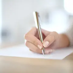 Main d'une personne écrivant avec un stylo sur un document.
