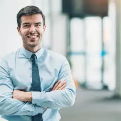 Un homme d'affaires souriant, bras croisés, incarne le rôle de mandataire social avec assurance.