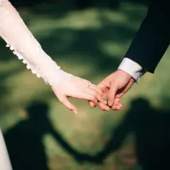 Mains jointes, une promesse scellée, un contrat universel d'amour éternel. La dentelle de la robe de mariée et le costume sombre symbolisent leur union.