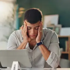 Un homme stressé se tient la tête devant une tablette.