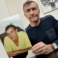 Un homme tient une photo d'un jeune homme en t-shirt jaune. Il semble chercher des réponses, se demandant sans nouvelle d'une personne que faire.