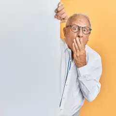 Homme âgé surpris, main sur la bouche, derrière un panneau blanc.