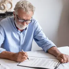 Un homme âgé signe un document, peut-être un modèle de lettre pour annuler un testament.