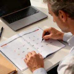 Un homme planifie ses congés sabbatiques dans son agenda, entouré d'un ordinateur portable et de post-it.