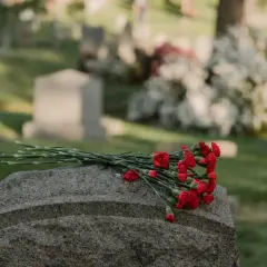 Un bouquet de fleurs rouges repose sur une pierre tombale dans un cimetière. Une question se pose : peut-on acheter une concession de son vivant ?