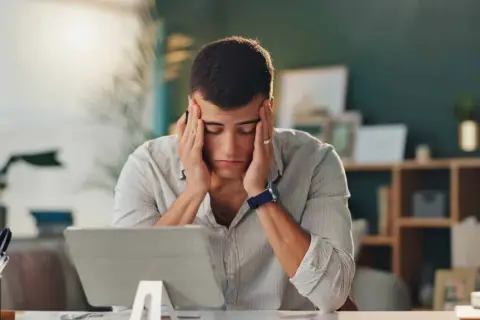 Un homme stressé se tient la tête devant une tablette.