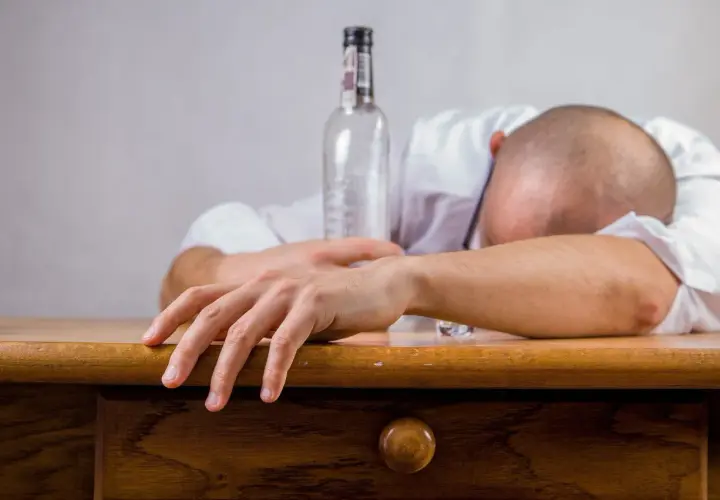 Un homme endormi sur son bureau, une bouteille vide à côté. Les conséquences de l'alcool au travail sont visibles.