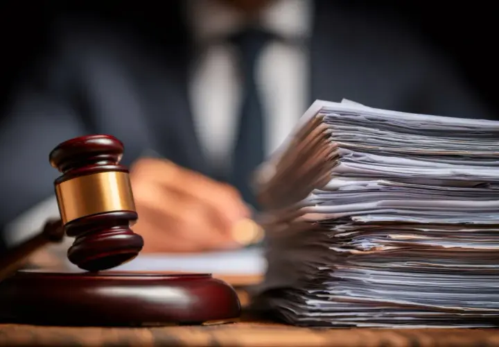 Marteau de juge et pile de documents, symbolisant la reddition de compte et la justice. Un homme en costume écrit en arrière-plan.