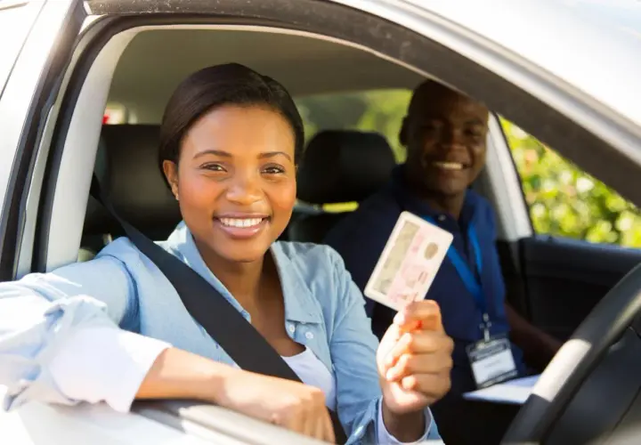 Une jeune femme souriante tient son permis de conduire, fière de sa réussite. L'auto-école veille à la répression des fraudes pour des formations honnêtes.