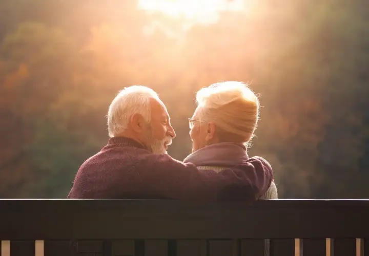 Couple âgé regardant le soleil couchant, bras autour des épaules.