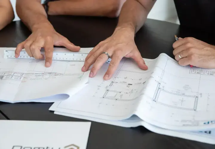 Des mains travaillent sur des plans d'architecte, une règle à la main. Comprendre ces détails est essentiel pour savoir pourquoi faire un devis précis.
