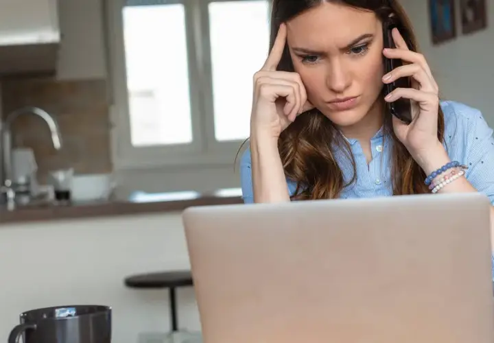 Femme soucieuse au téléphone, devant son ordinateur, envisageant de porter plainte contre une entreprise.