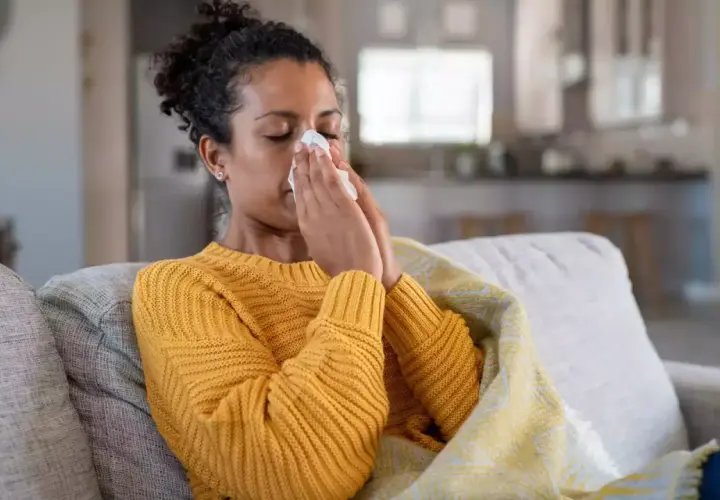 Femme malade sur un canapé, se mouchant dans un mouchoir. Elle est couverte d'une couverture. Cela pourrait être un arrêt maladie pendant préavis démission.