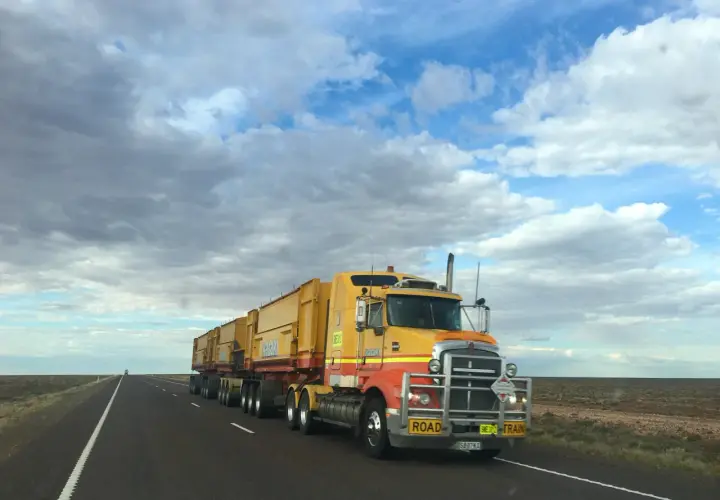 Un long camion jaune, un "road train", roule sur une route déserte sous un ciel nuageux. Ce véhicule est essentiel pour la convention collective transport.