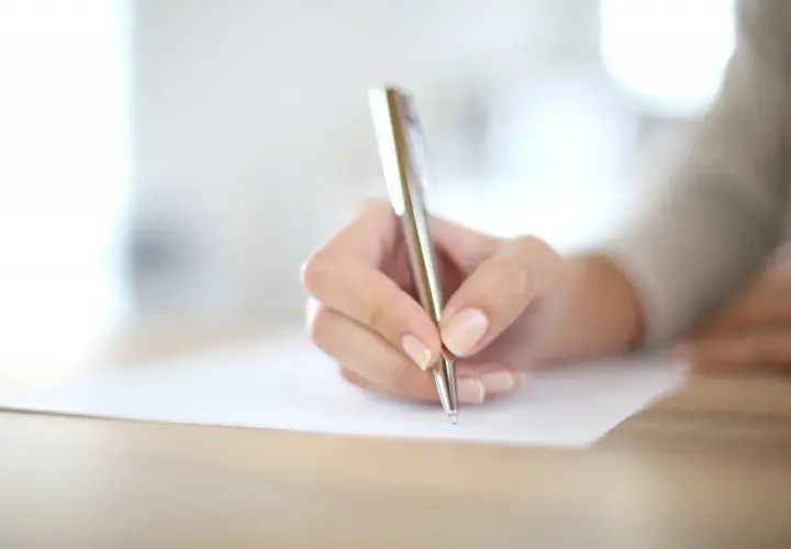 Main d'une personne écrivant avec un stylo sur un document.