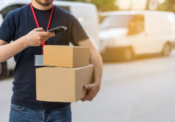 Livreur avec colis, vérifiant son téléphone. Un retard de livraison peut être une violation du code de la consommation.
