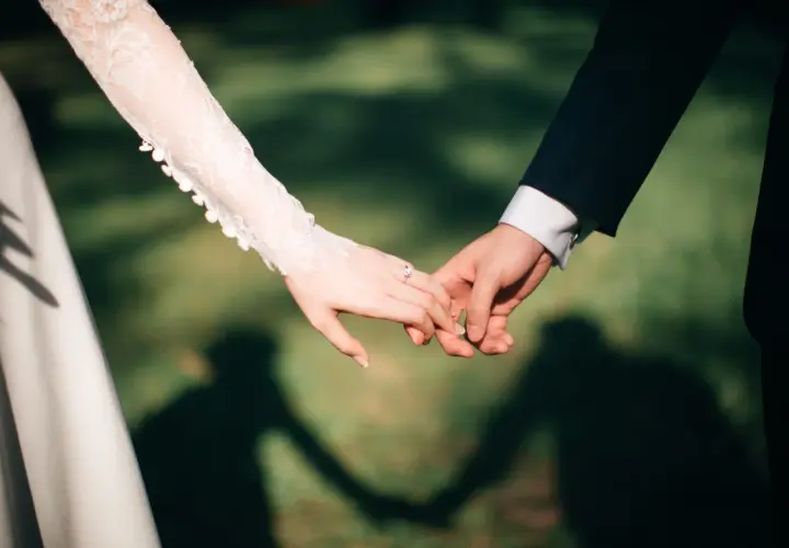 Mains jointes, une promesse scellée, un contrat universel d'amour éternel. La dentelle de la robe de mariée et le costume sombre symbolisent leur union.