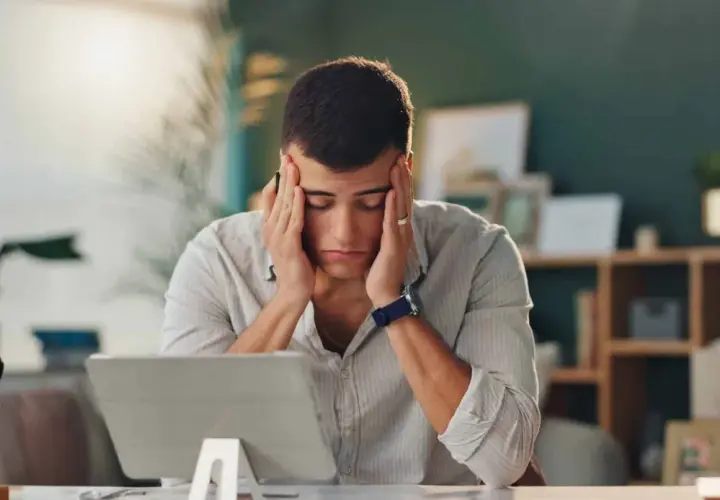 Un homme stressé se tient la tête devant une tablette.