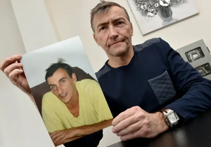 Un homme tient une photo d'un jeune homme en t-shirt jaune. Il semble chercher des réponses, se demandant sans nouvelle d'une personne que faire.