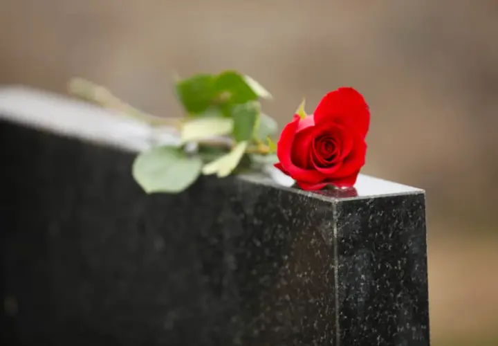 Une rose rouge sur une pierre tombale, symbole de deuil et de souvenir. Le notaire s'occupe du déblocage des fonds succession.