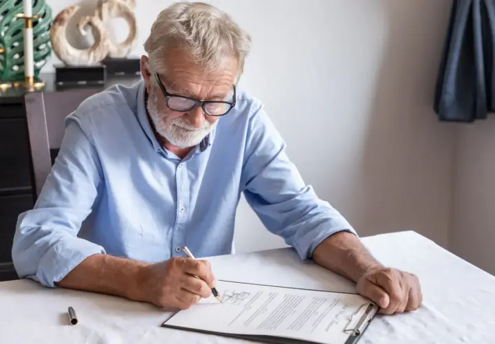 Un homme âgé signe un document, peut-être un modèle de lettre pour annuler un testament.