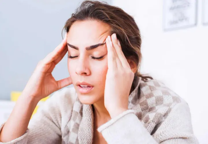 Femme se tenant les tempes, l'air soucieux. Comment toucher 100 % de son salaire en arrêt maladie ?
