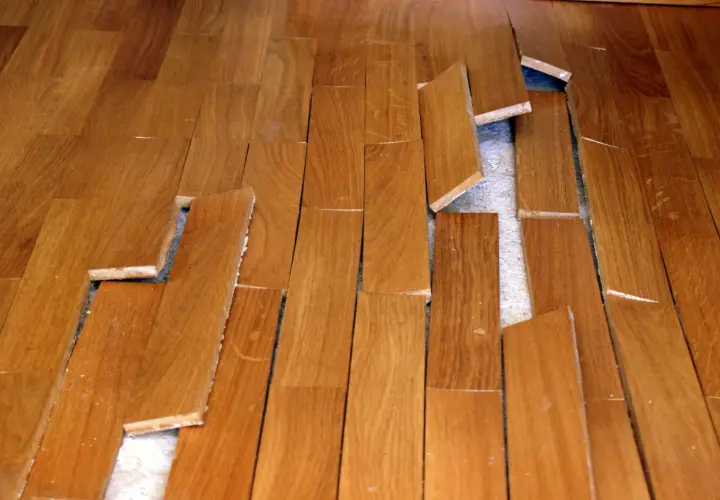 Parquet en bois abîmé, lames décollées et cassées. Une vraie malfaçon de travaux qui rend le sol dangereux.