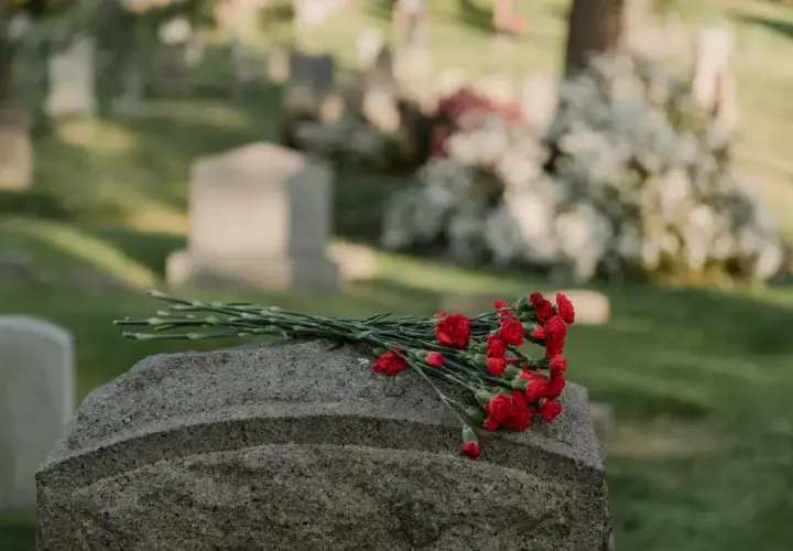Un bouquet de fleurs rouges repose sur une pierre tombale dans un cimetière. Une question se pose : peut-on acheter une concession de son vivant ?
