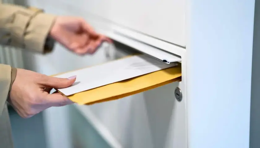 Main tenant insère des enveloppes dans une boîte aux lettres. Le délai recommandé pour la réception est important.