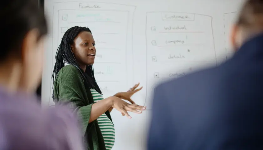 Une femme enceinte présente un tableau blanc, discutant peut-être de la réduction du temps de travail pendant la grossesse.