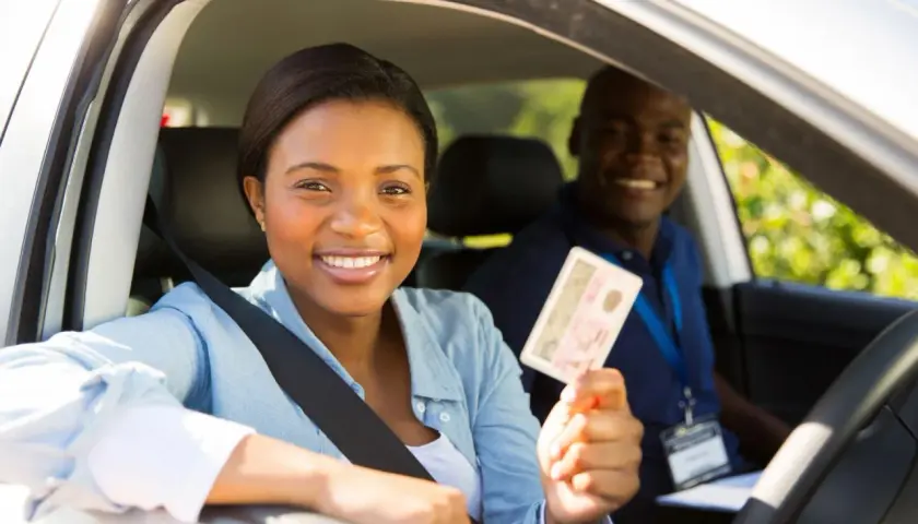 Une jeune femme souriante tient son permis de conduire, fière de sa réussite. L'auto-école veille à la répression des fraudes pour des formations honnêtes.