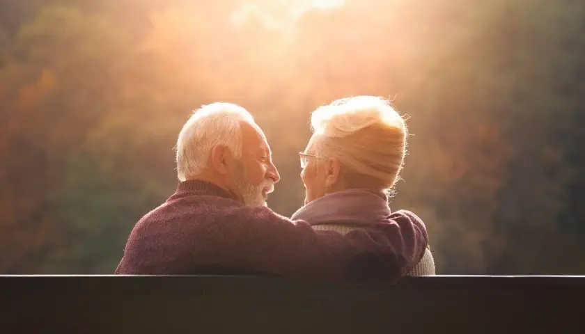 Couple âgé regardant le soleil couchant, bras autour des épaules.