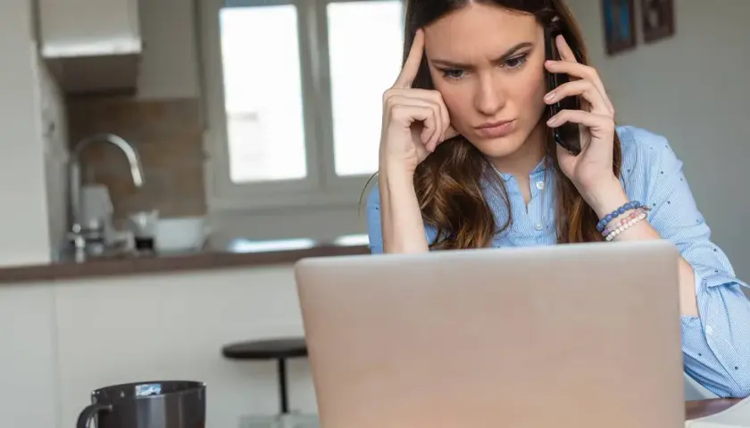 Femme soucieuse au téléphone, devant son ordinateur, envisageant de porter plainte contre une entreprise.