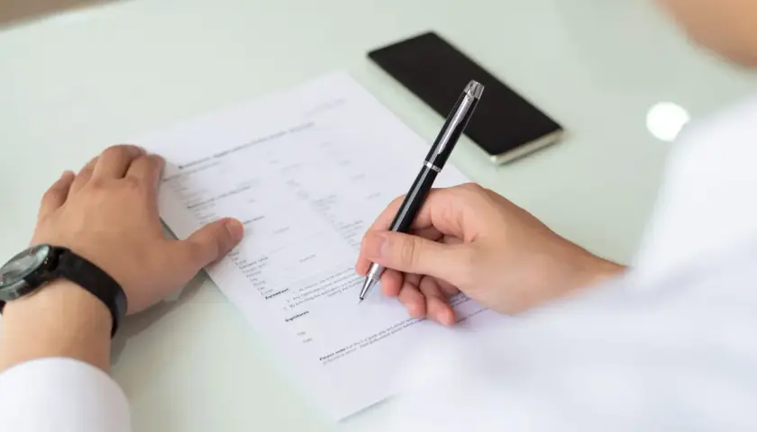 Un homme remplit un formulaire, peut-être un cerfa, pour une demande. Il utilise un stylo pour signer.