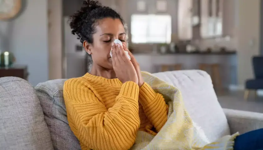 Femme malade sur un canapé, se mouchant dans un mouchoir. Elle est couverte d'une couverture. Cela pourrait être un arrêt maladie pendant préavis démission.