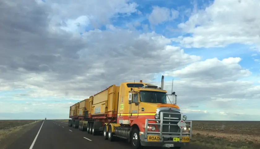 Un long camion jaune, un "road train", roule sur une route déserte sous un ciel nuageux. Ce véhicule est essentiel pour la convention collective transport.