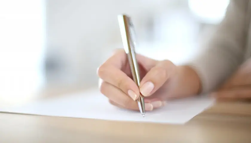 Main d'une personne écrivant avec un stylo sur un document.