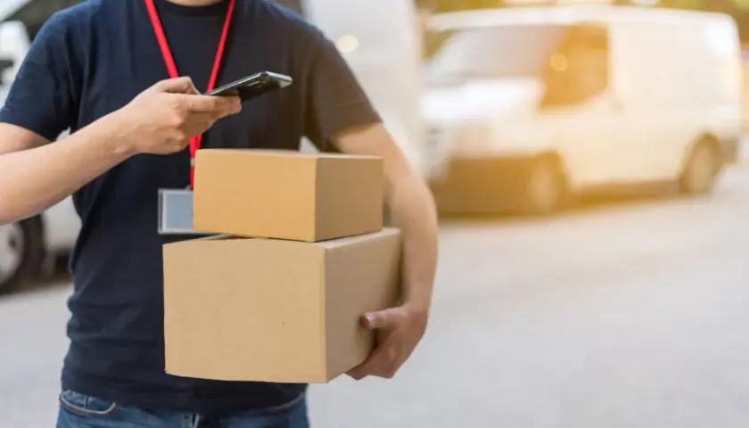 Livreur avec colis, vérifiant son téléphone. Un retard de livraison peut être une violation du code de la consommation.