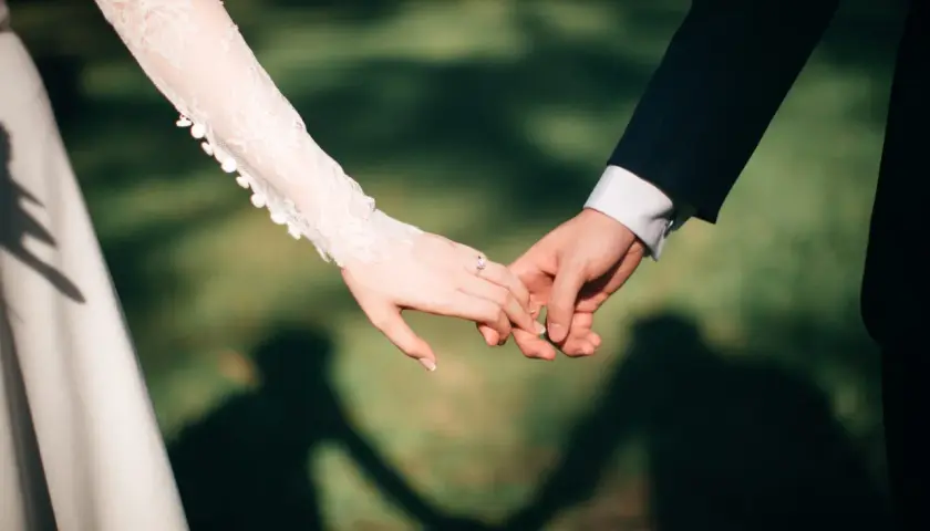 Mains jointes, une promesse scellée, un contrat universel d'amour éternel. La dentelle de la robe de mariée et le costume sombre symbolisent leur union.